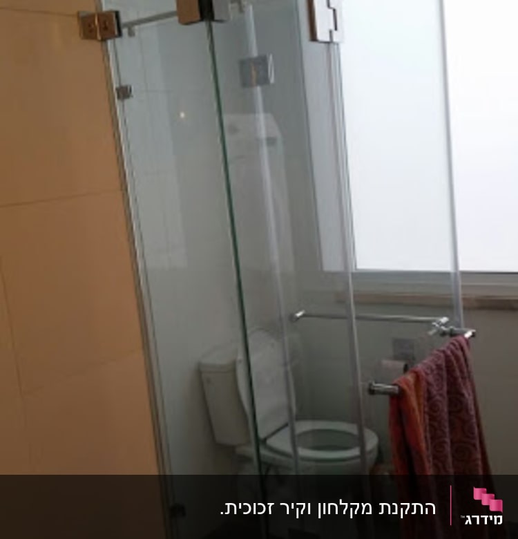 מקלחון זכוכית עם דלתות שקופות ומגבת תלויה